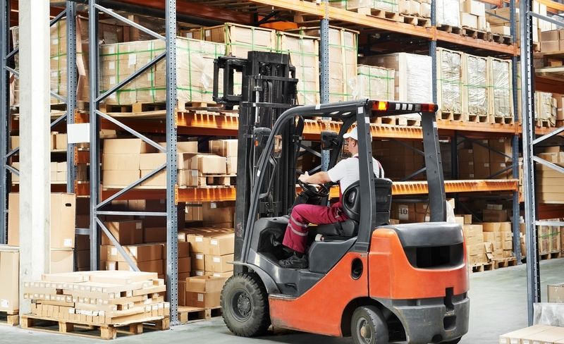 Gabelstaplerfahrer hebt Paletten mit Kartons in einem Lager mit hohen Regalen