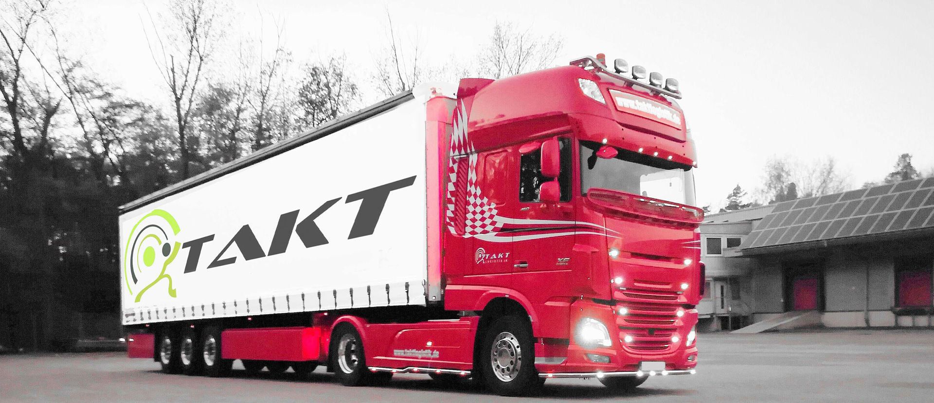 Roter Sattelzug mit weißem Anhänger und Aufschrift 'TAKT' vor Lagergebäude mit Solarpanelen
