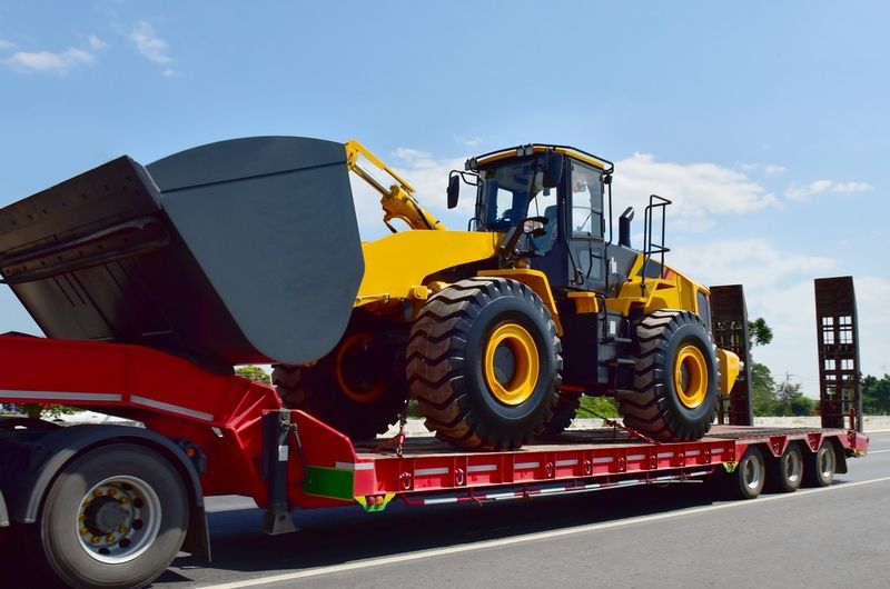 Gelber Radlader mit großem Schaufel auf rotem Tieflader auf Straße